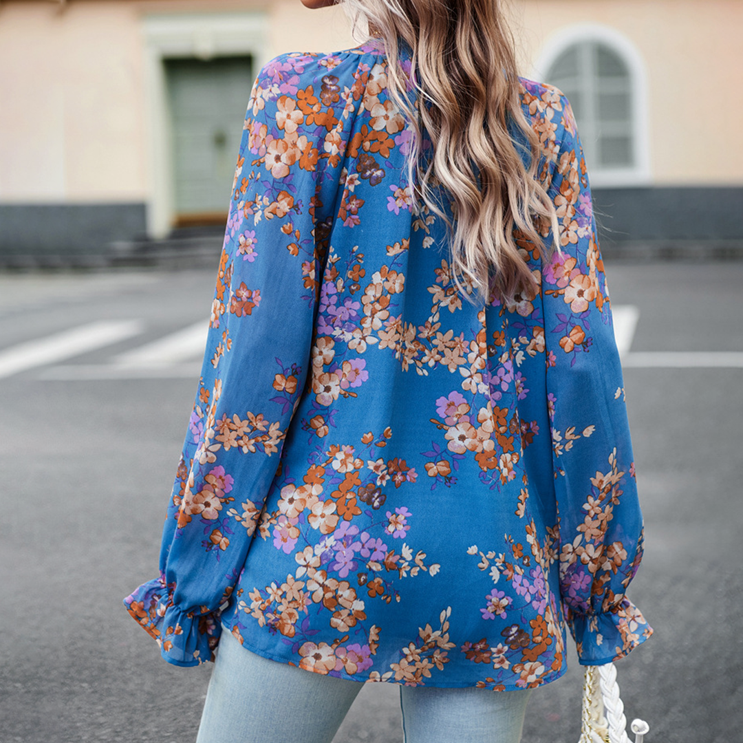 Frau in blauer, geblümter Bluse aus Chiffon, Rückansicht, lässiger Stil, Straße im Hintergrund.