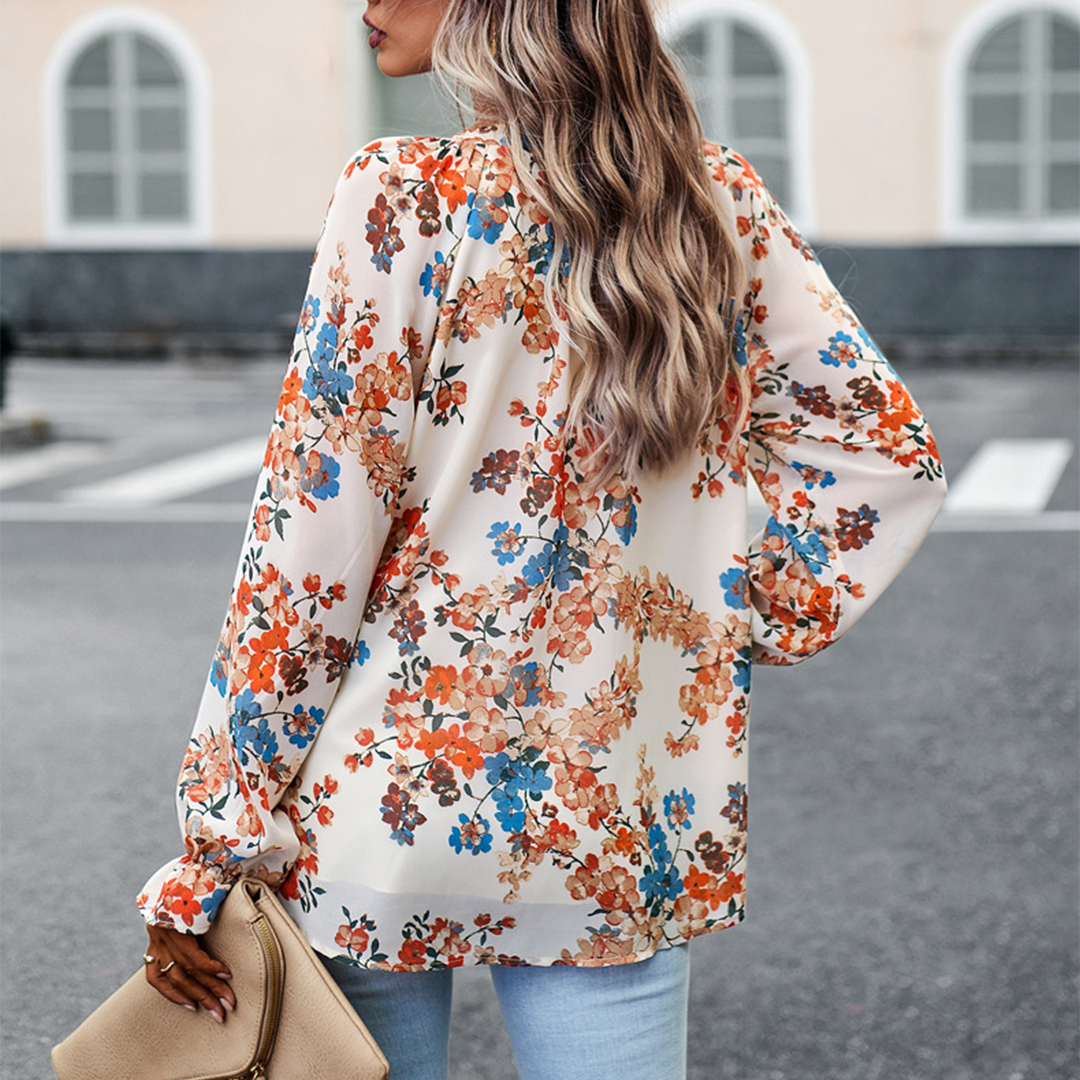 Frau in blumiger Bluse, beige Tasche, blonde Haare, Stadtstraße, modisch, lässiger Stil.
