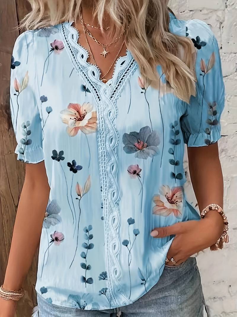 Frau in hellblauer Bluse mit Blumenmuster, Spitzenbesatz, kurzen Ärmeln, lässiger Sommerlook.
