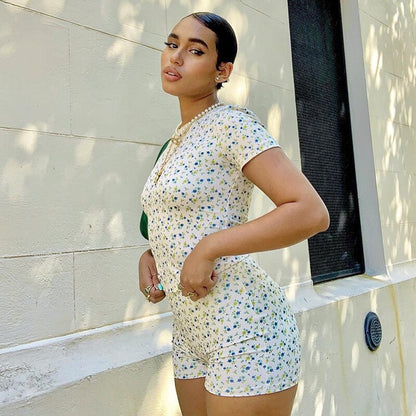 Frau in geblümtem Jumpsuit, weiß-blau, Sommermode, draußen, vor heller Wand.