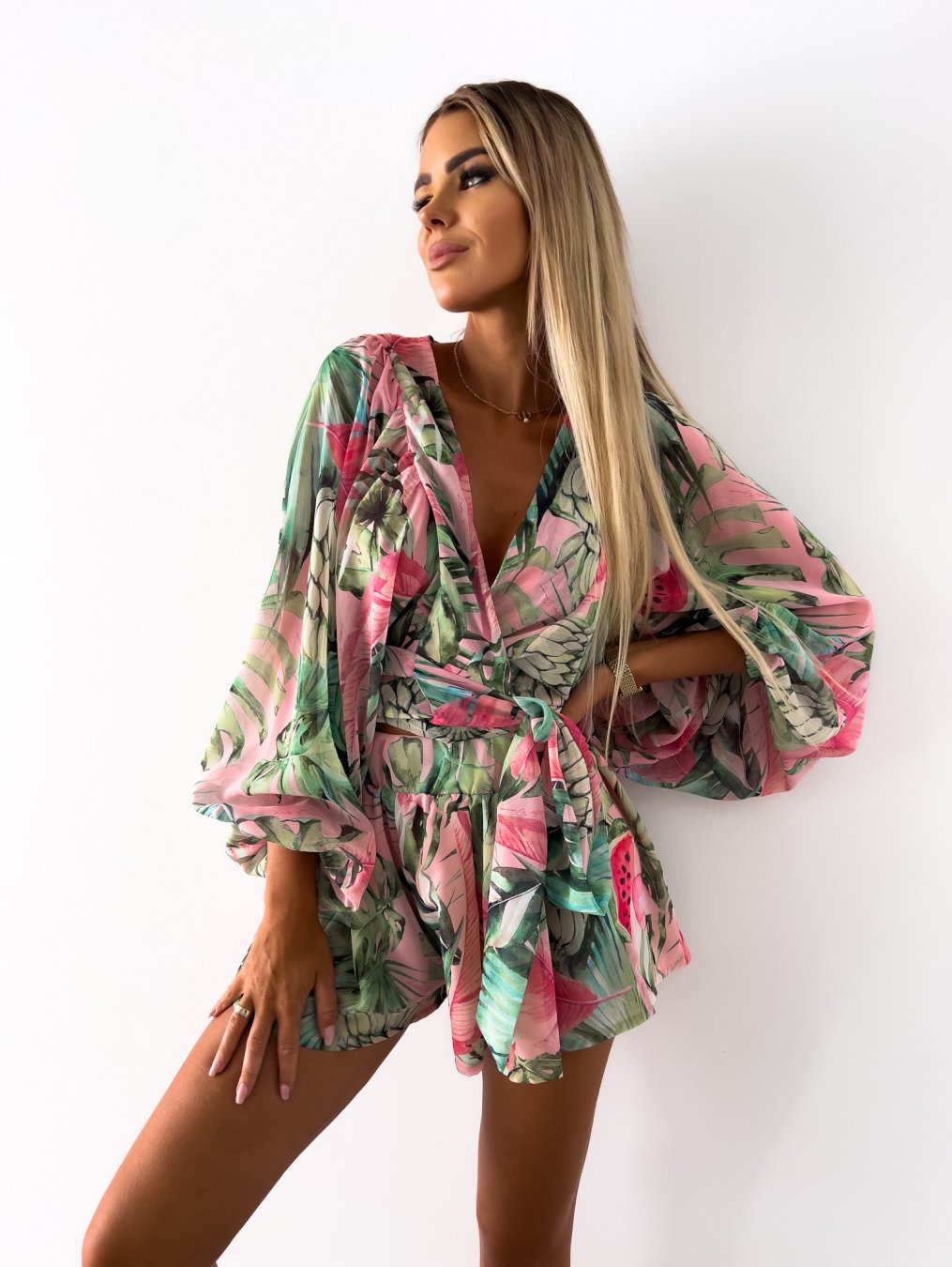 Frau in grün-rosa Sommerkleid mit tropischem Muster, V-Ausschnitt, weite Ärmel, modisch.