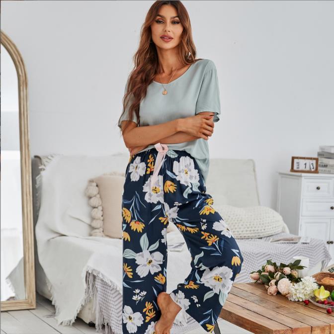 Frau in blauer Blumenhose und grünem Shirt, steht in modernem Wohnzimmer, Mode, Freizeitkleidung.
