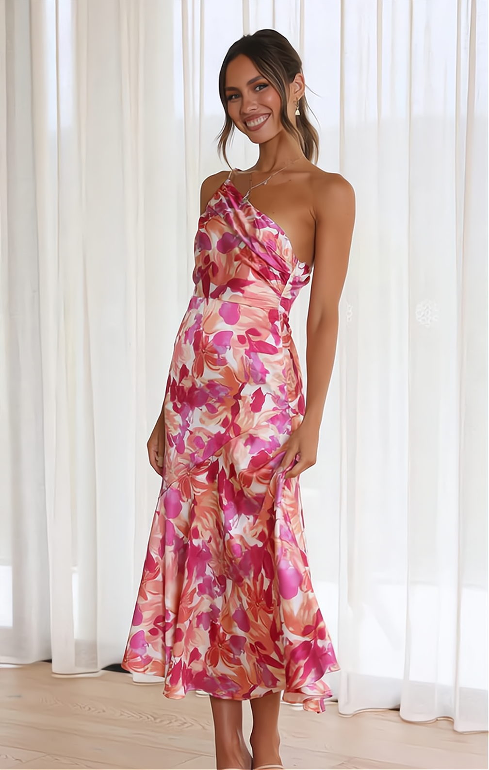 Frau in rosa geblümtem Satin-Kleid, ärmellos, knielang, vor weißen Vorhängen stehend.