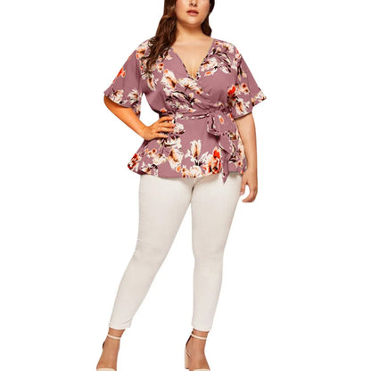 Frau in lila Blumenbluse mit Gürtel und weißen Hosen, Mode für große Größen, elegant und modern.