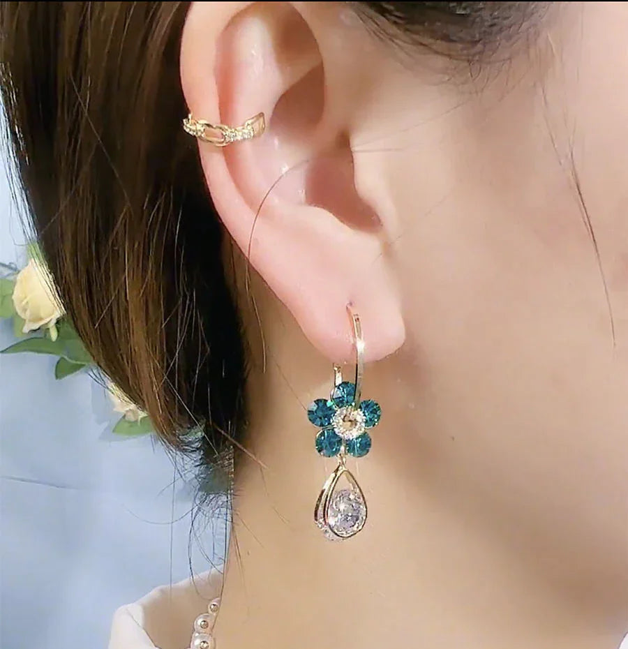 Frau mit goldenen Ohrringen, blauen Blumenanhängern und Ohrklemme, eleganter Schmuck.