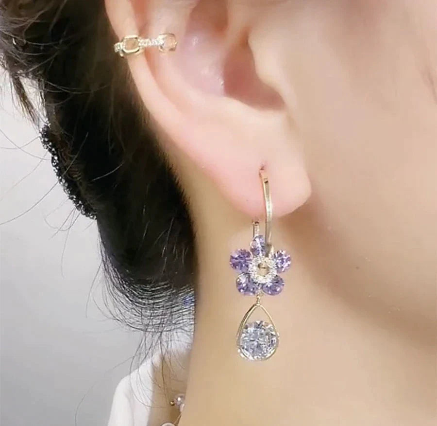Frau mit lila Blumenohrring und Ohrstecker, eleganter Schmuck, Nahaufnahme.
