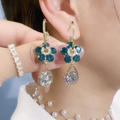 Goldene Ohrringe mit blauen Blumen und Kristallanhängern, eleganter Schmuck für Damen.