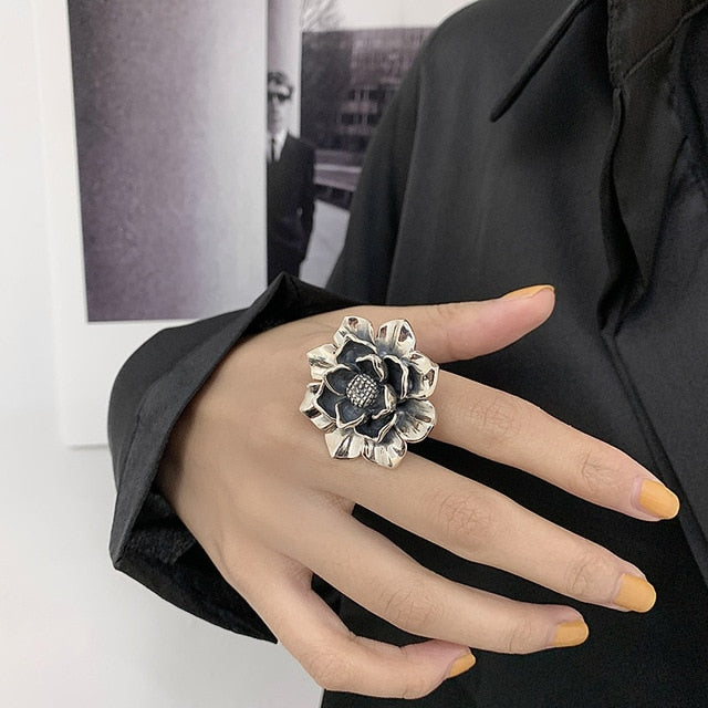 Silberner Blumenring an Hand, schwarzes Blütenzentrum, elegantes Schmuckdesign, Damenmode.