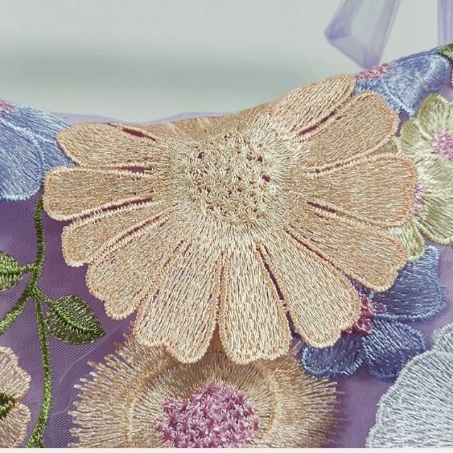 Blumenstickerei auf lila Stoff, pastellfarben, detailliert, dekorativ, Textildesign.