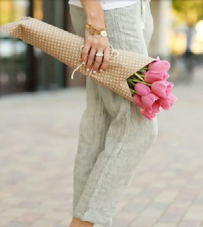 Frau hält Strauß rosa Tulpen in gepunktetem Papier, Frühlingsblumen, Geschenkidee.