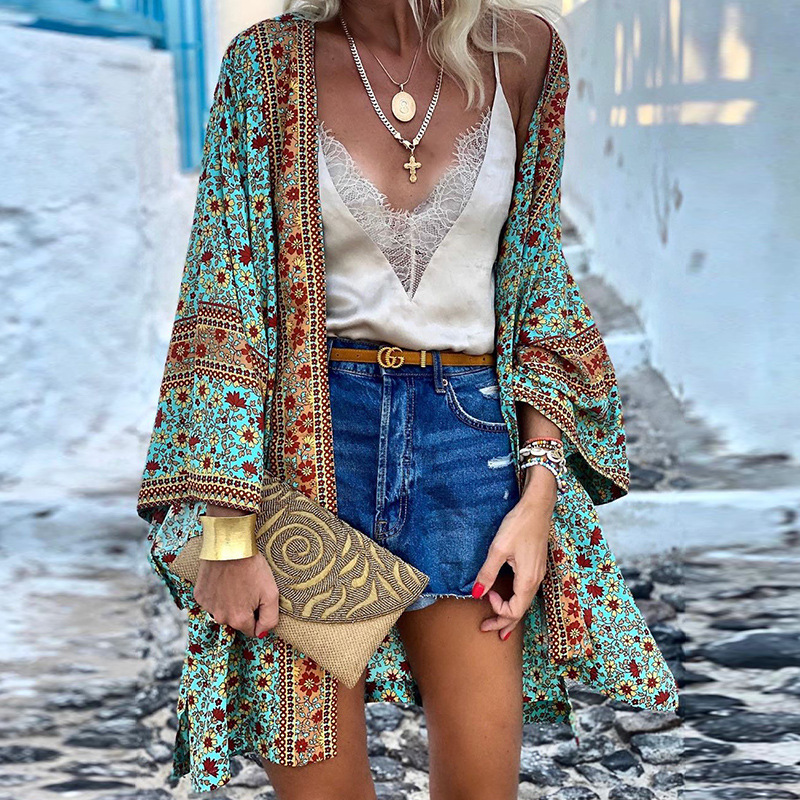 Frau in Boho-Kimono, blau-rot gemustert, mit Jeansshorts und goldener Clutch auf gepflasterter Straße.