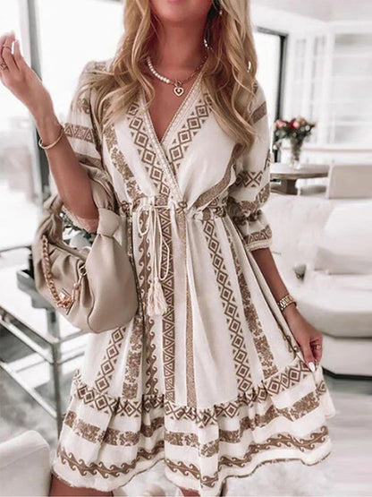 Frau in weißem Boho-Kleid mit geometrischem Muster, beige Handtasche, elegantes Wohnzimmer.
