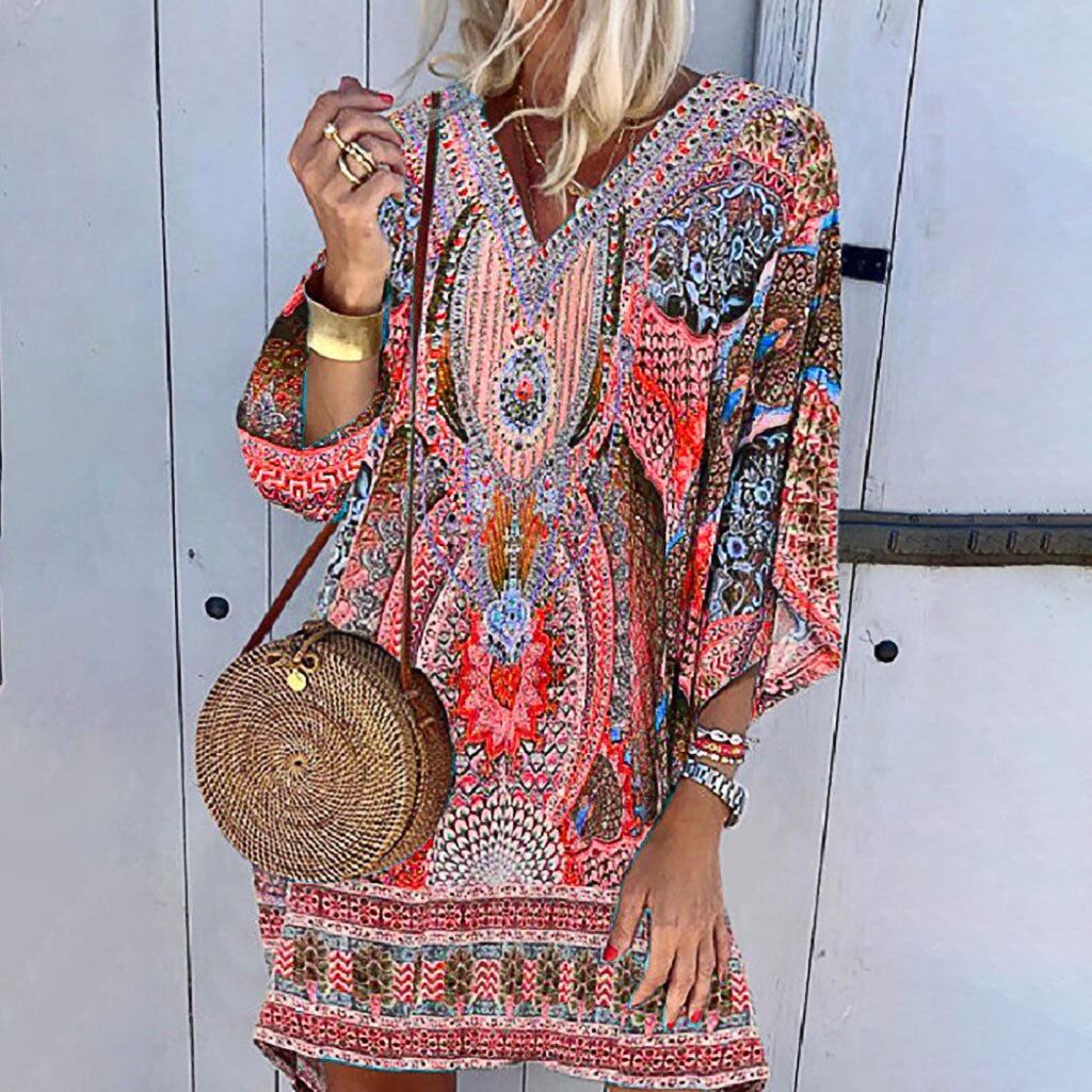Frau in bunter Boho-Minikleid mit langen Ärmeln, runde Strohtasche, lässiger Sommerlook.