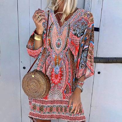 Frau in bunter Boho-Minikleid mit langen Ärmeln, runde Strohtasche, lässiger Sommerlook.