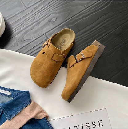 Braune Wildleder-Schlupfclogs auf Holzboden, modisch, bequem, ideal für Herbstmode.