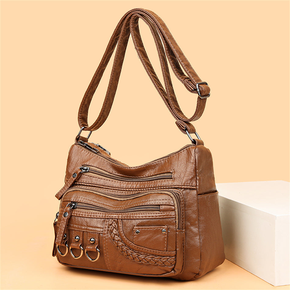 Braune Lederhandtasche mit mehreren Reißverschlusstaschen und verstellbarem Schulterriemen.