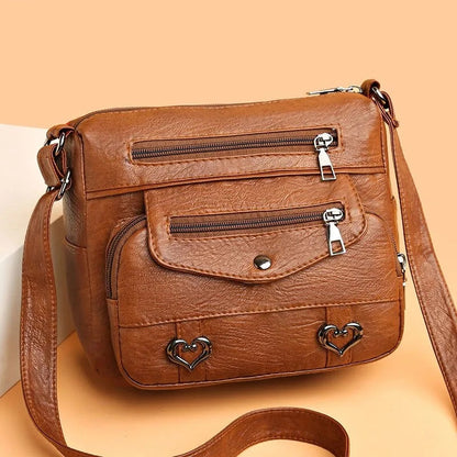 Braune Damen-Umhängetasche aus Leder mit Reißverschlusstaschen und Herzdetails.