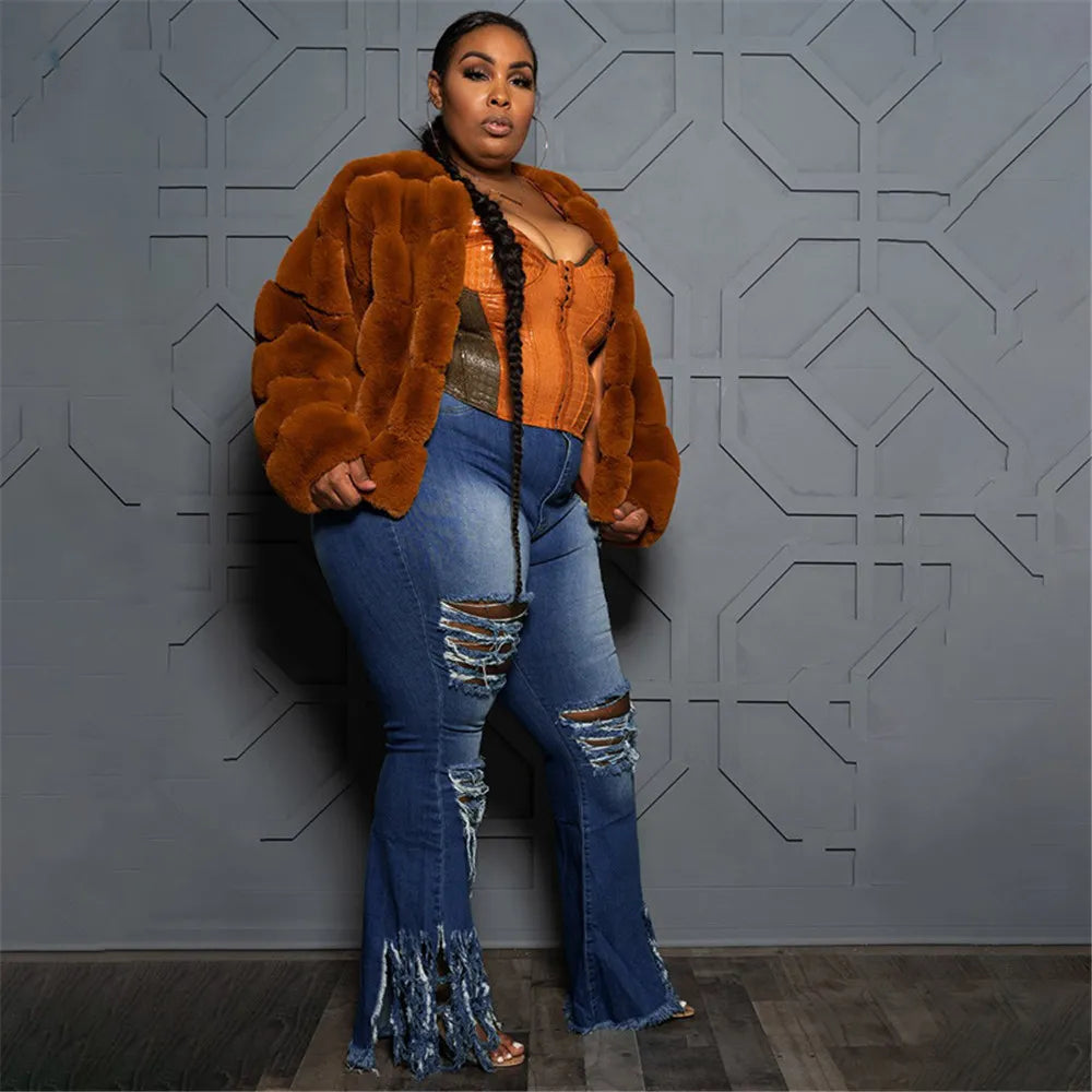 Frau in brauner Kunstpelzjacke, zerrissene Jeans, vor grauer geometrischer Wand.