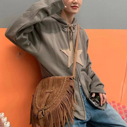 Frau mit brauner Wildleder-Fransentasche, grauem Kapuzenpullover und blauer Jeans.