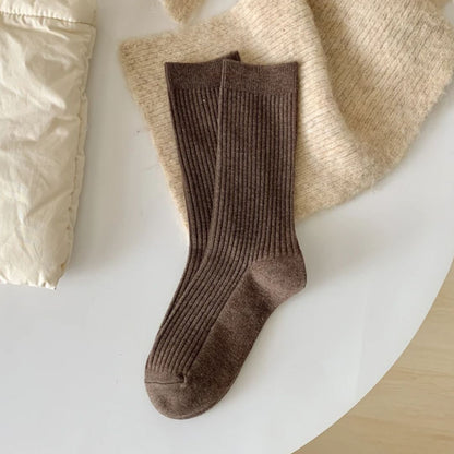 Braune Stricksocken aus Wolle auf beigem Stoff, gemütliche Wintermode, warme Accessoires.
