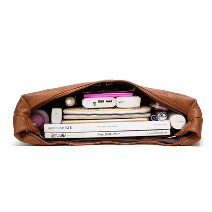 Braune Ledertasche mit Zeitschriften, Powerbank und Kosmetikartikeln, ideal für Reisen.