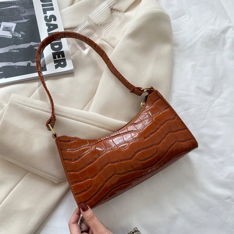 Braune Handtasche aus Krokodillederimitat auf weißem Hintergrund, modisch und elegant.