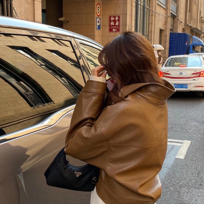 Frau in brauner Lederjacke mit schwarzer Prada-Tasche neben Auto auf Stadtstraße.