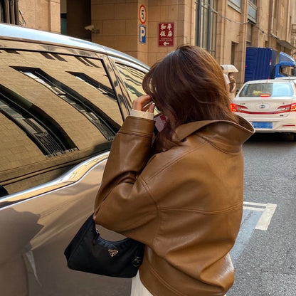 Frau in brauner Lederjacke mit schwarzer Prada-Tasche neben Auto auf Stadtstraße.
