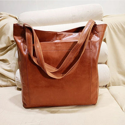 Braune Ledertasche auf beigem Sofa, modisch, geräumig, ideal für Alltag und Büro.