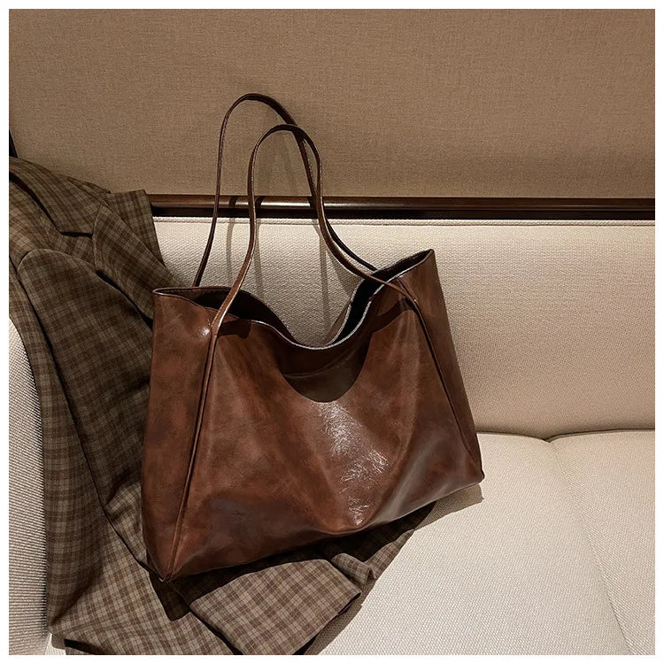 Braune Ledertasche auf kariertem Mantel, stilvoll, geräumig, für Damen, modisches Accessoire.