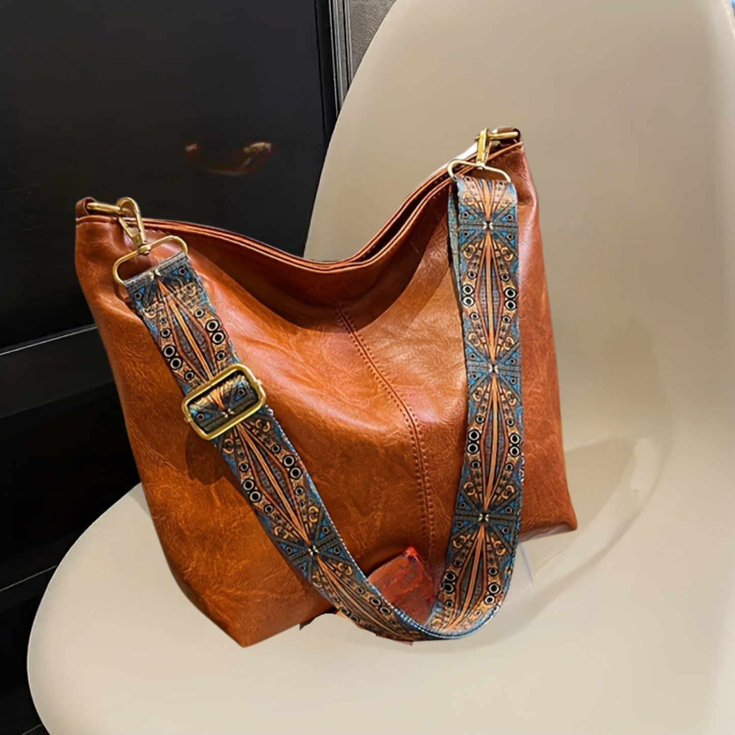 Braune Ledertasche mit gemustertem Schultergurt auf Stuhl, modisches Accessoire.