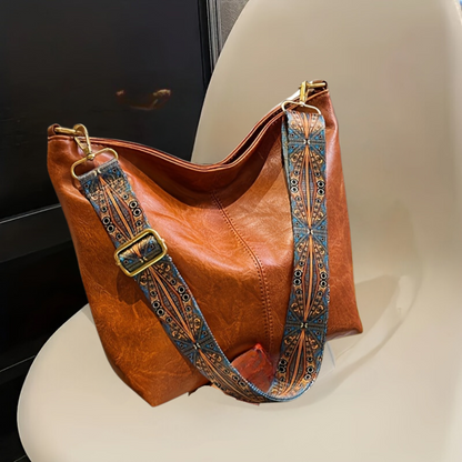 Braune Ledertasche mit gemustertem Schultergurt auf Stuhl, modisches Accessoire.