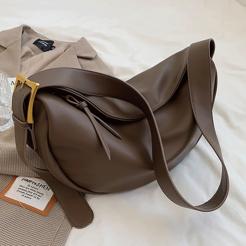 Braune Lederhandtasche mit goldener Schnalle auf beigem Blazer, modisch und elegant.