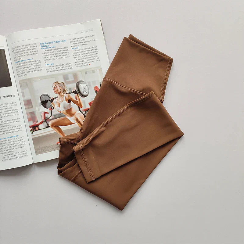 Braune Sportleggings aus Stretchmaterial auf weißem Hintergrund neben Fitnessmagazin.
