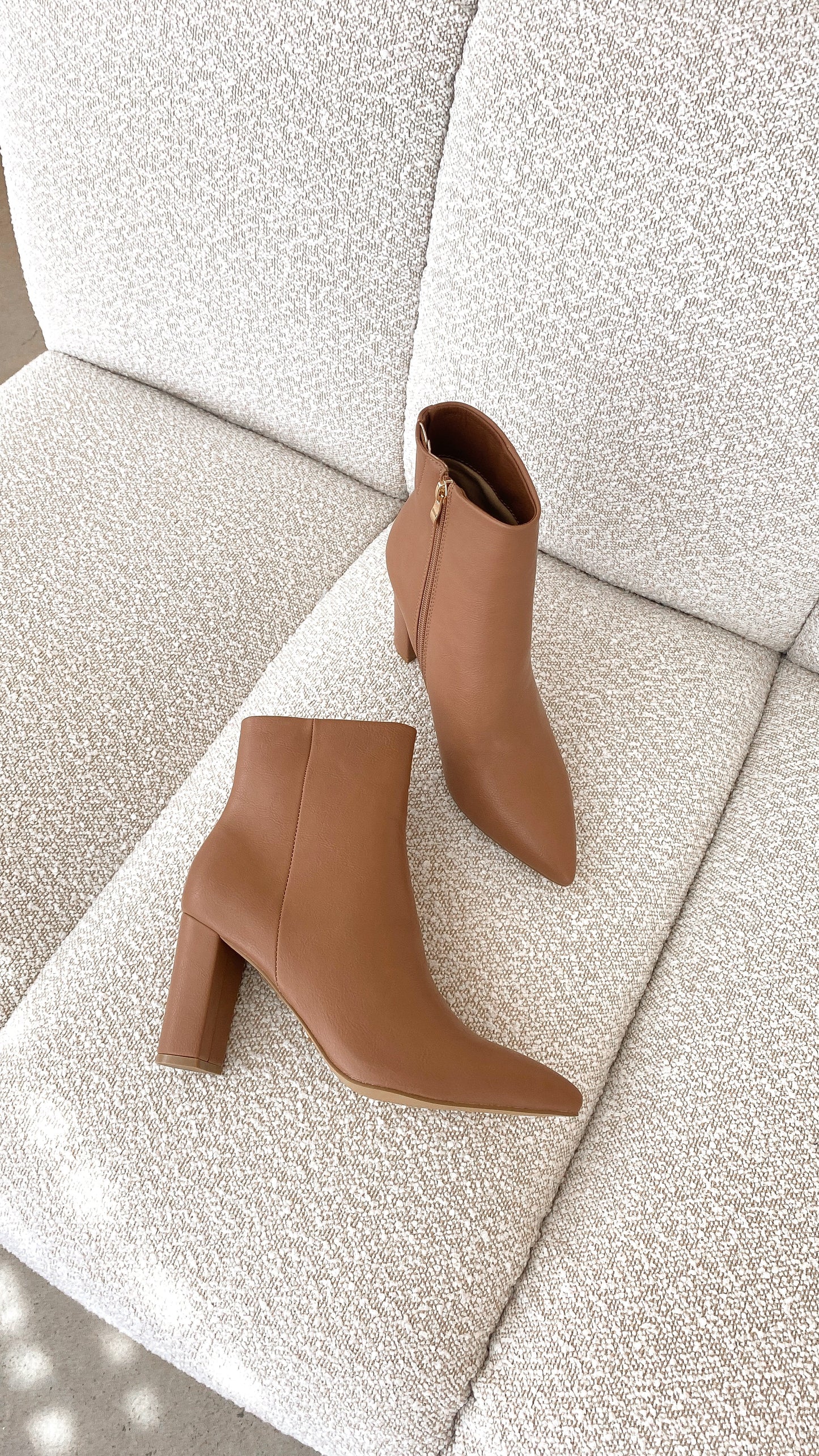 Braune Damen-Stiefeletten aus Leder mit Blockabsatz auf beigem Sofa, modisch und elegant.