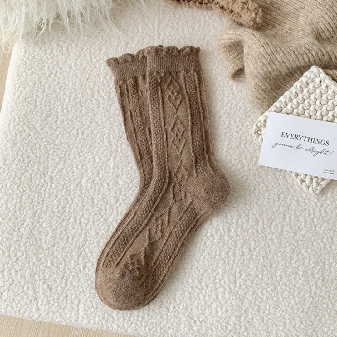 Braune Stricksocke mit Zopfmuster auf weißem Hintergrund, gemütliche Wintermode.