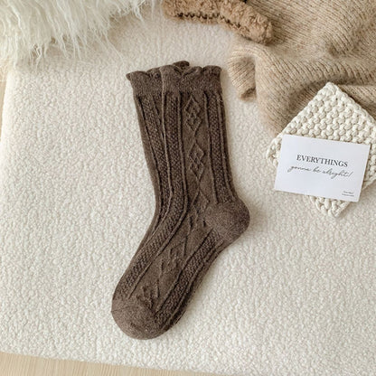 Braune Stricksocken aus Wolle mit Zopfmuster auf weißem Hintergrund, gemütliche Wintermode.