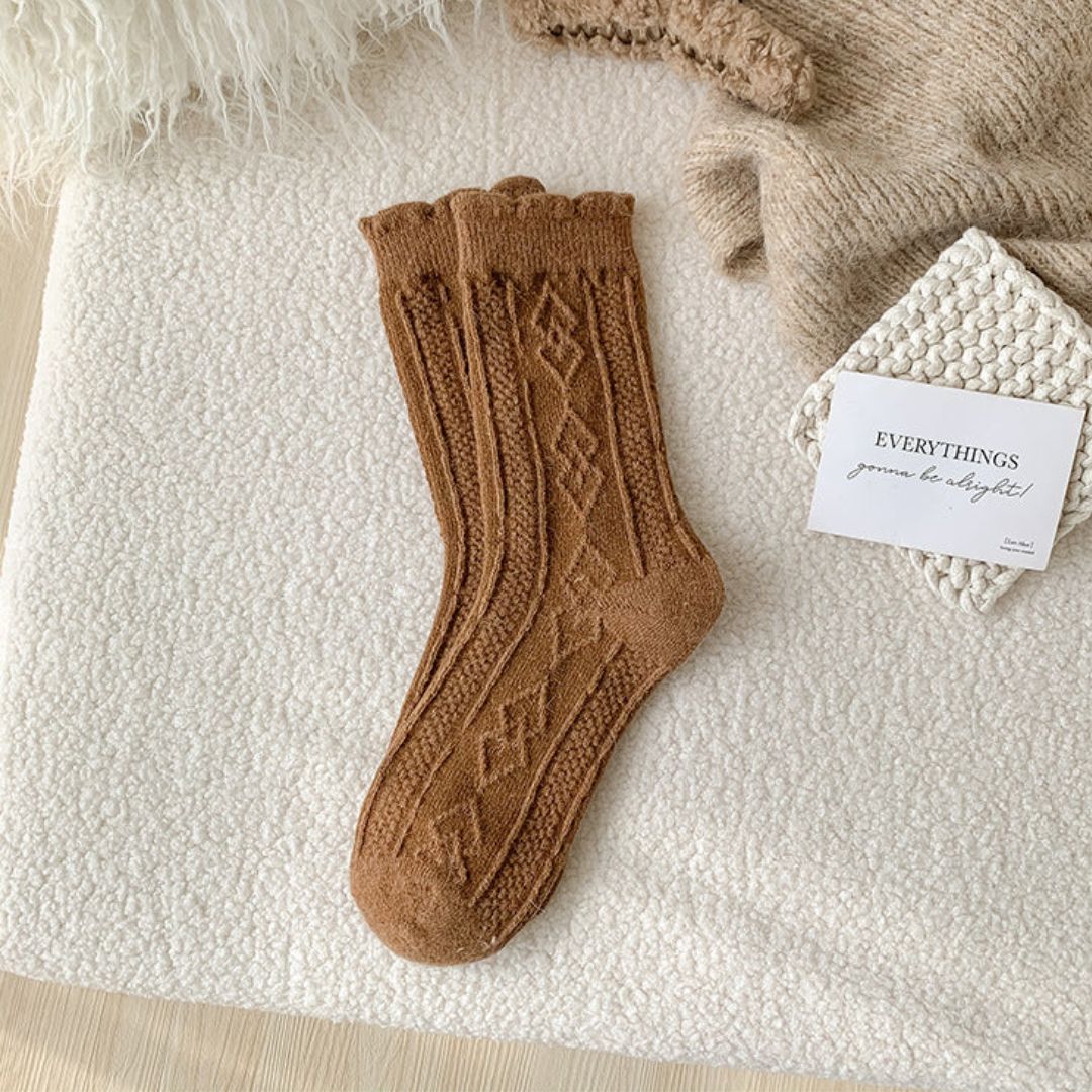 Braune Stricksocken mit Zopfmuster auf weißem Hintergrund, gemütliche Wintermode.