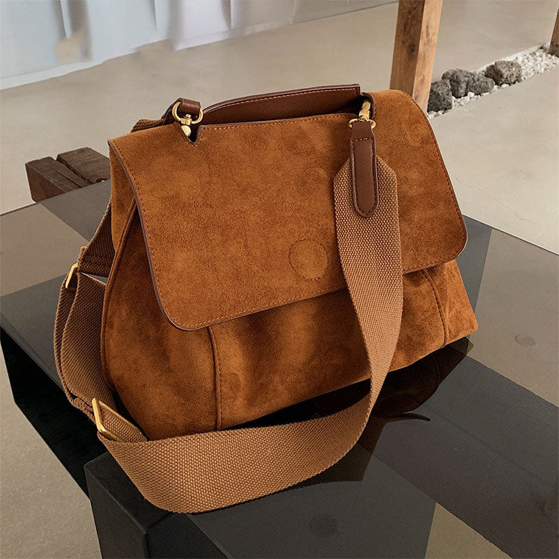 Braune Wildleder-Handtasche mit verstellbarem Schultergurt auf Glastisch.