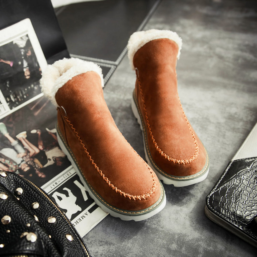 Braune Wildleder-Winterstiefel mit weißem Fellfutter auf grauem Hintergrund.