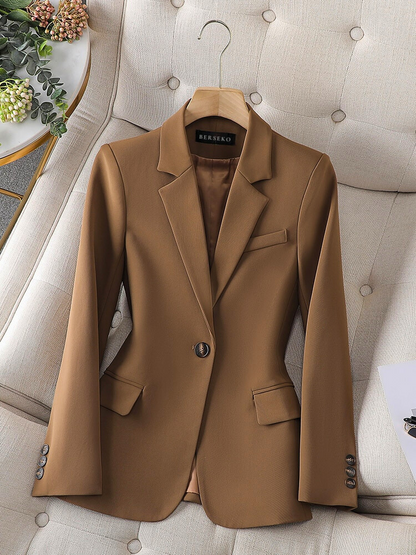 Eleganter brauner Damenblazer aus Wolle, einreihig, mit Knöpfen, auf beigem Sessel.