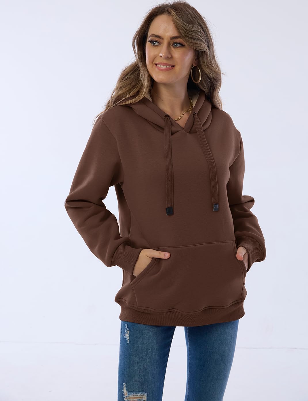 Frau in braunem Kapuzenpullover, lässig, modisch, mit Kängurutasche, Jeans, Freizeitkleidung.