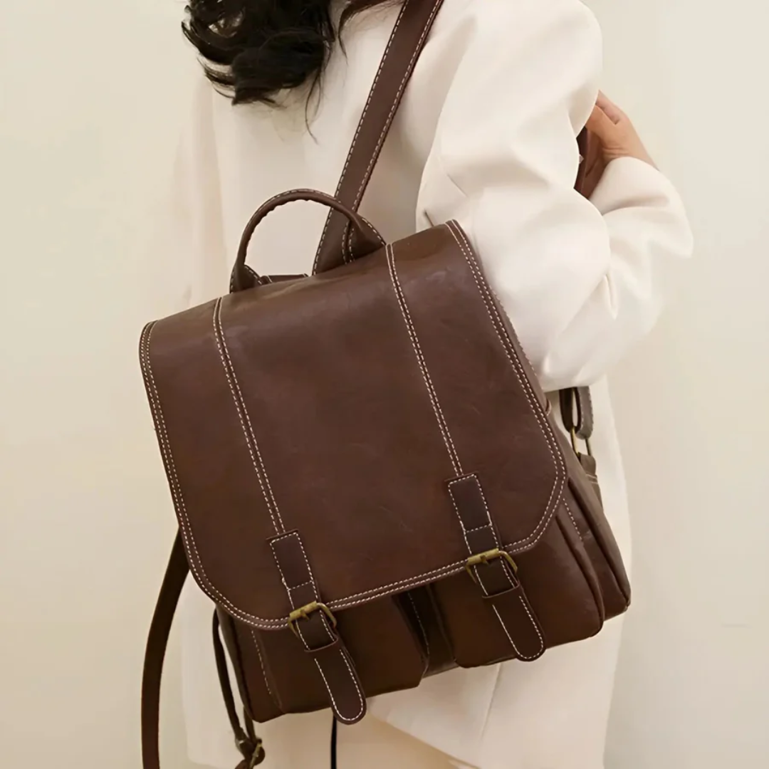 Dunkelbrauner Lederrucksack, Vintage-Stil, mit Schnallen, getragen von Person in weißem Mantel.