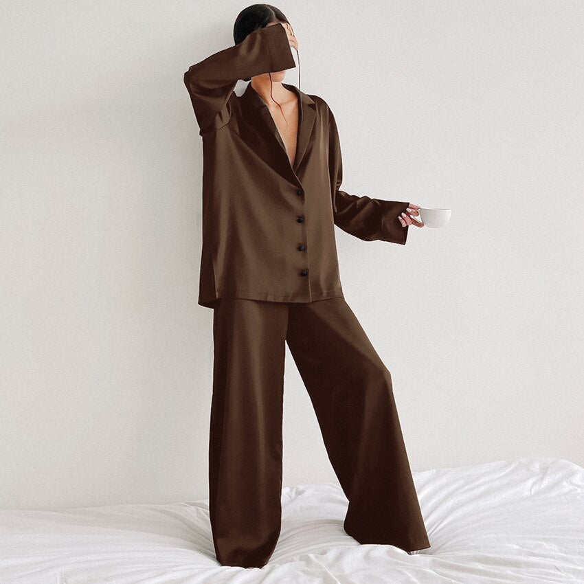 Frau in braunem Satin-Pyjama mit Tasse, elegantes Nachtwäsche-Set, Schlafzimmer-Hintergrund.