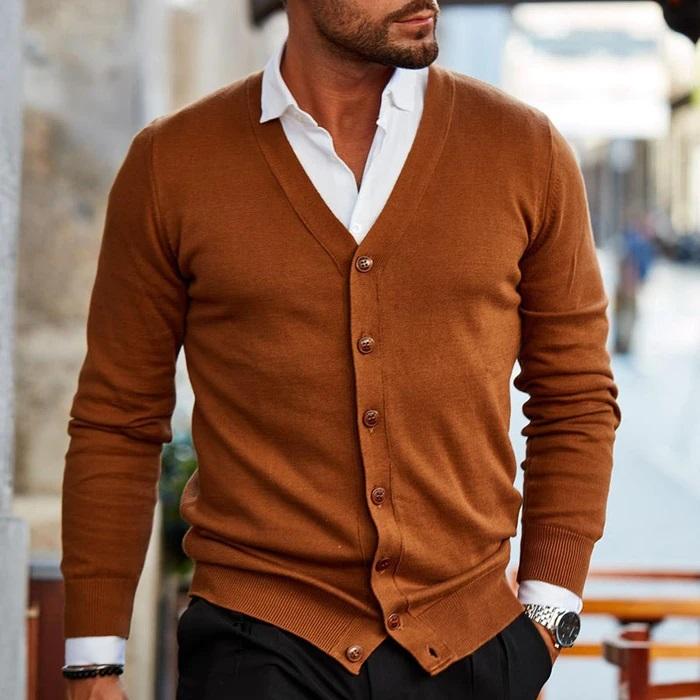 Mann in braunem Cardigan, weißem Hemd, schwarze Hose, stilvolle Herrenmode, urbane Kulisse.