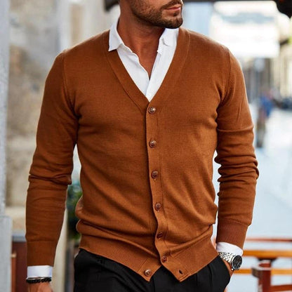 Mann in braunem Cardigan, weißem Hemd, schwarze Hose, stilvolle Herrenmode, urbane Kulisse.