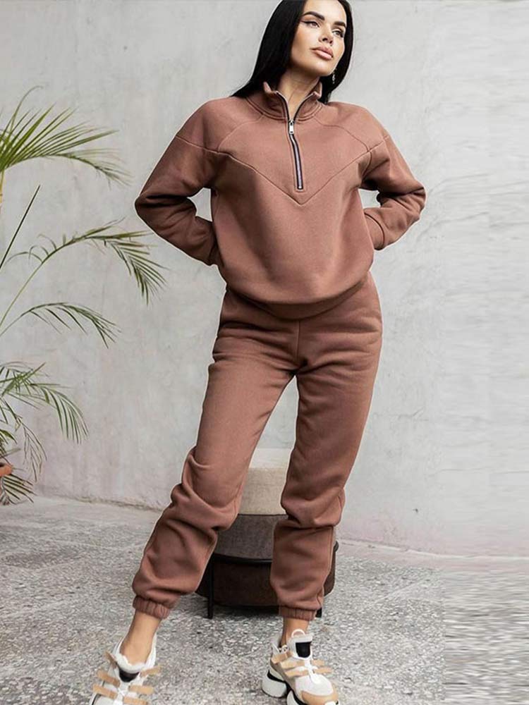 Frau in braunem Jogginganzug, Reißverschluss, Freizeitmode, bequeme Kleidung, Indoor-Pflanze.