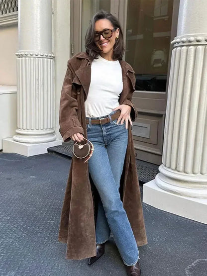 Frau in braunem Wildledermantel, weißem Shirt, blauer Jeans, braunen Stiefeln, Sonnenbrille.