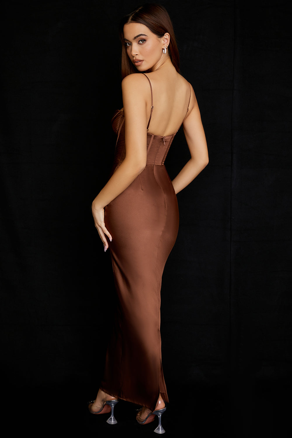 Frau in braunem Satin-Abendkleid mit Spaghettiträgern, elegantes Design, schwarze Kulisse.