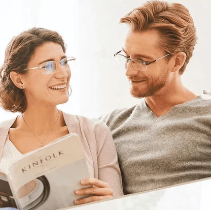Zwei Personen mit Brillen lesen ein Magazin auf einem Sofa, lächelnd und entspannt.